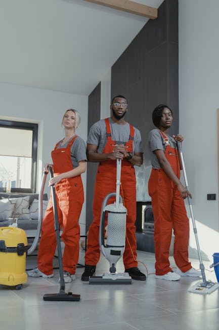 Three professional cleaning staff from Harrow Weald Carpet Cleaners standing in a modern living room during a commercial cleaning service. They are wearing matching grey shirts and bright orange overa