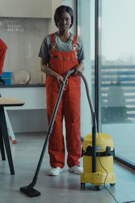 Three professional cleaning staff from Harrow Weald Carpet Cleaners standing in a modern living room during a commercial cleaning service. They are wearing matching grey shirts and bright orange overa